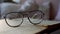 Closeup of a hand putting optical glasses on an old book, glass table in slow motion