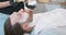 Closeup hands of female barber, who applies with brush shaving cream on young bearded man's face and neck