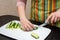 Closeup hands girl is left handed in a striped apron in the kitchen is slicing cucumbers into strips on a whiteBoard on