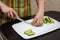 Closeup hands girl in a striped apron in the kitchen is slicing cucumbers into strips on a whiteBoard on the black table
