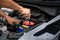 Closeup, The hands of a male technician are using a tool to replace the car battery, parked at home. Black car, the battery is