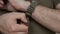Closeup of the hands of men in khaki clothes, are removed from the wrist watch on nylon strap.