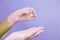 Closeup of hands in pink gloves with pipette and drop of transparent oil on lilac background