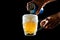 Closeup of the hands pouring a beer from a can into a glass on the black background