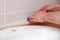 Closeup hands of professional plumber worker applying white sealant, joint compound, caulk to joint of wooden table top, beige