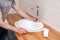 Closeup hands of a professional plumber worker installs a white oval ceramic sink on a wooden tabletop in the bathroom with beige