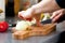 Closeup of the hands of a woman cook slicing onion on a wooden board.