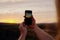 Closeup of hands of young woman holding mobile taking picture of morning sunrise
