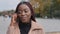 Closeup headshot happy attractive African American young woman standing outdoor in autumn holding smartphone, charming