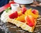 Closeup honey waffle with strawberry and peach and icing sprinkle on black plate