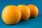 Closeup of a horizontal row of three vibrant orange oranges on light blue background