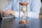 Closeup hourglass on table, businesswoman working on laptop on background