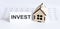 Closeup of house wooden model with blank for text INVEST on chart background