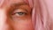 Closeup of human female eye with pink hair. Woman with natural face beauty makeup isolated over pink background