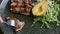 Closeup human hands cut off one slice of grilled meat by fork and knife on black plate