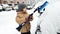 Closeup image of boy in beige coat clean up the car after snow storm with brush