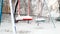 Closeup image of empty snow covered playground after blizzard. Blue and red swing under snow