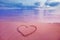 Closeup image of heart symbol written on sand at pink sunrise