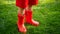 Closeup image of ittle boy in red rubber wellington boots standing on green grass lawn
