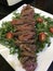 Closeup image of a plate of seared sliced steak on a bed of rocket served with cherry tomatoes