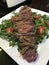 Closeup image of a plate of seared sliced steak on a bed of rocket served with cherry tomatoes