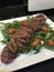 Closeup image of a plate of seared sliced steak on a bed of rocket served with cherry tomatoes