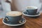 Closeup image of two blue cups of hot latte coffee and Americano coffee on vintage wooden table