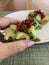 Closeup image of a woman holding a half eaten slice of sourdough avocado toast topped with pomegranate arils