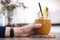 Closeup image of a woman`s hand holding a glass of orange cold brew coffee on wooden table
