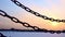 Closeup of iron chain guardrail on frozen lake, ice rink at sunset in winter