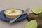 Closeup of a key lime tartlet and a fork on a blue plate with key lime fruits on a wooden board