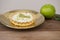 Closeup of a key lime tartlet on a plate and a key lime fruit on a wooden board