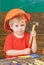 Closeup kid in orange helmet holding hammer in his hands. Crafts lesson at kindergarten. Portrait of little boy in