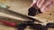 Closeup of knife cuts sausage. Scene. Close-up of cutting dark salami on wooden cutting board. Salt on background of