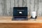 Closeup laptop with inscription on screen e-learning and image of square academic cap and cup of coffee on bench. Online education