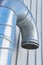 Closeup of a large metal ventilation pipe against the side of a building outside. Engineered stainless steel extractor