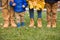 Closeup of legs of a family standing on green grass and holding bunches of yellow marple leaves outdoors on autumn day