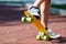 Closeup of the legs and yellow skateboard. Boy rising a board on two wheels, focus on skate.