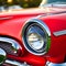 Closeup on the lights and grill to one side of a red classic car, AI Generated