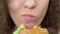 Closeup of the lips. Woman eats a juicy hamburger, hands in black rubber gloves