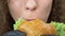 Closeup of the lips. woman eats a juicy hamburger, hands in black rubber gloves