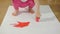 Closeup of a little girl with her hands dirty in red paint draws her fingers on a large sheet of white paper sitting on