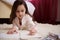 Closeup little girl in pajamas, lying down on carpet in bedroom, concentrated on drawing picture with colorful pencils