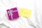 closeup of a little yellow note with handwritten i love you on white sheets of the bed and a giftbox, valentines concept