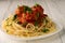 Closeup of a lone plate with cooked spaghetti with meatballs seasoned with parsley, on a white wooden table