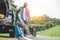 Closeup lower body of Asian couple relaxing on SUV car trunk with yellow trolly luggage along road trip with mountain hill