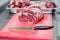 Closeup macro pieces ribeye marbled beef steak with knife on red plastic cutting board on metal table in restaurant kitchen.