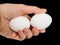 Closeup of a male hand, with a pair of white hen eggs