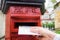 Closeup on a male hand putting a letter in a red letterbox. Concept of vintage type of communication.