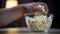 Closeup of male hand taking popcorn from bowl on table, unhealthy food addict